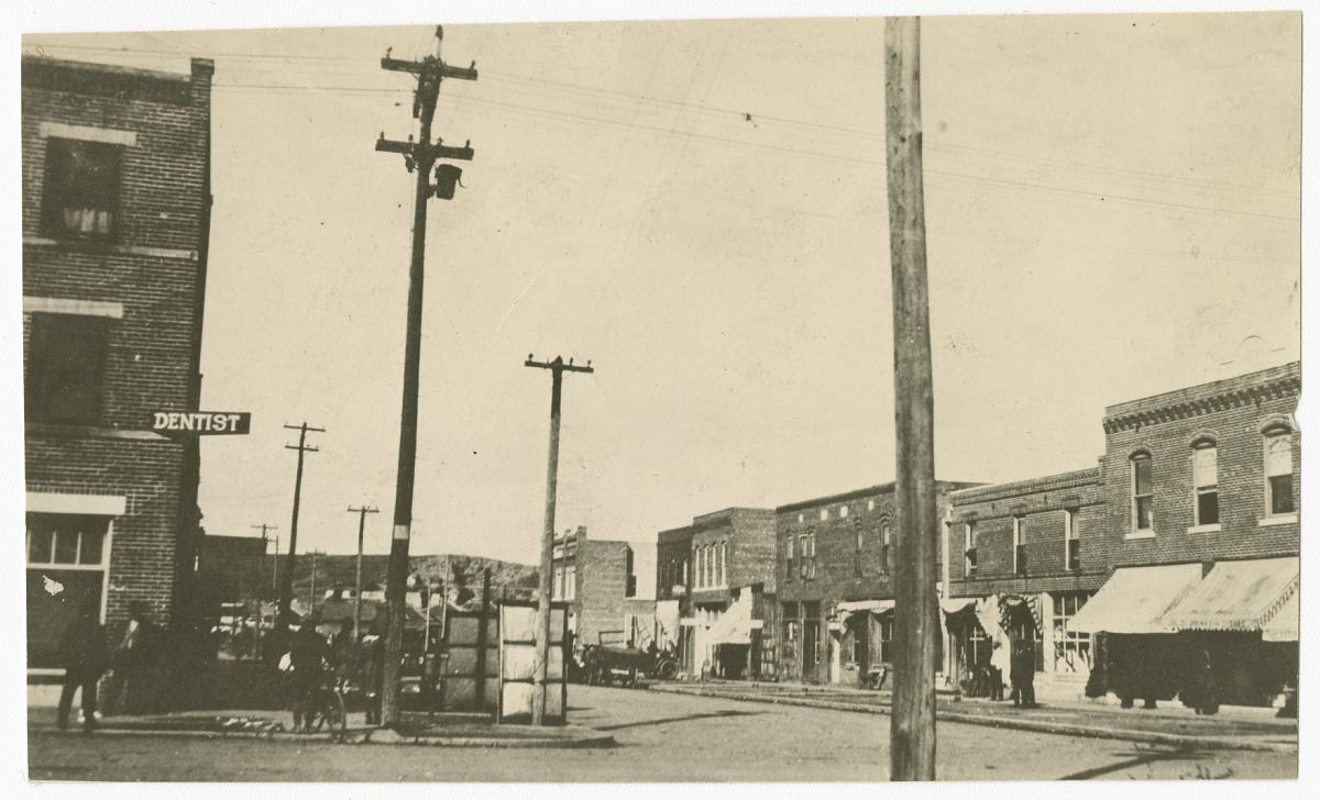 North Greenwood Avenue in Tulsa, Oklahoma, prior to the 1921 Tulsa Race Massacre — a row of brick storefronts including a dentist's office, with utility poles and pedestrians along the street